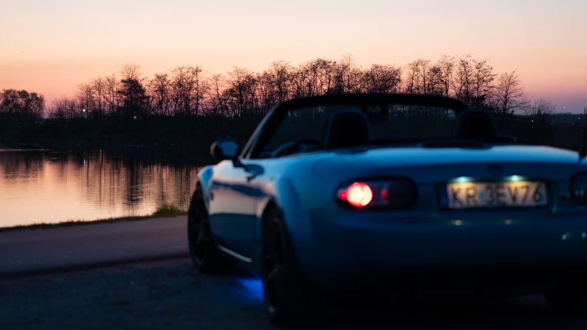 A blue convertible sports car parked by a serene lakeside during dusk in Brzegi, Poland.